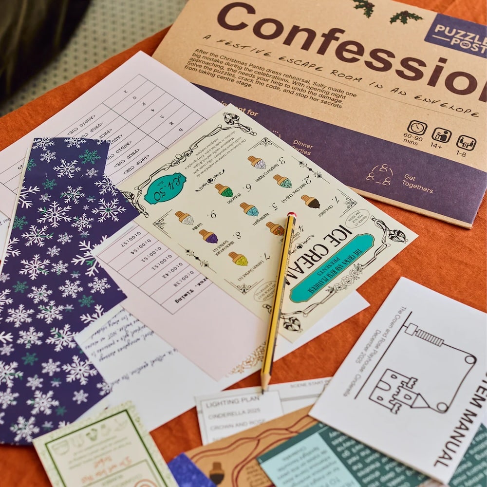 A tabletop scene with puzzle papers, an instruction sheet, a pencil, and a large envelope labeled Confession, suggesting an at-home escape room game setup. The papers feature charts, drawings, and colorful designs.