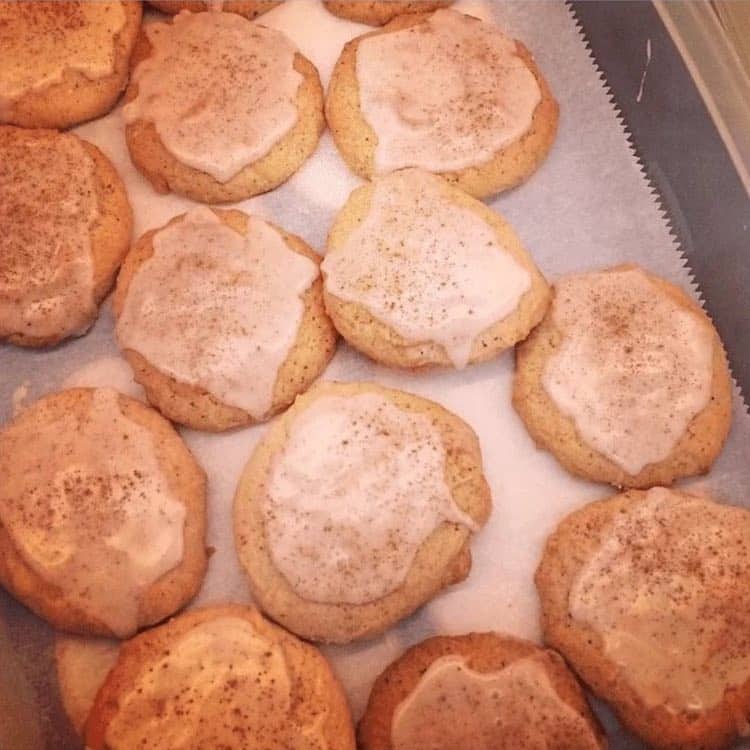 A batch of homemade cookies with a light glaze and a sprinkle of cinnamon on top, arranged on a sheet of parchment paper.