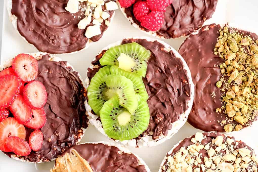 Assorted rice cakes topped with chocolate and a variety of toppings like strawberries, kiwi, raspberries, pistachios, chopped nuts, and peanut butter—perfect for after school snacks or as part of your favorite healthy snack recipes.