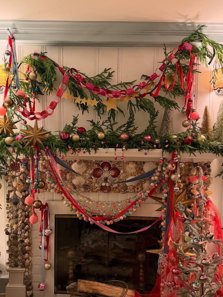 A fireplace decorated for Christmas with garlands, red and pink ribbons, colorful ornaments, gold stars, and festive trees creates a magical Christmas atmosphere—perfect inspiration for holiday DIY projects and cozy celebrations.