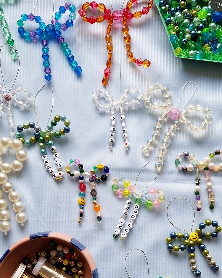 Colorful beaded dragonfly ornaments, some with letter beads spelling words like “peace,” “love,” and “kindness,” are arranged on a light surface. Nearby are bowls and trays filled with assorted beads.
