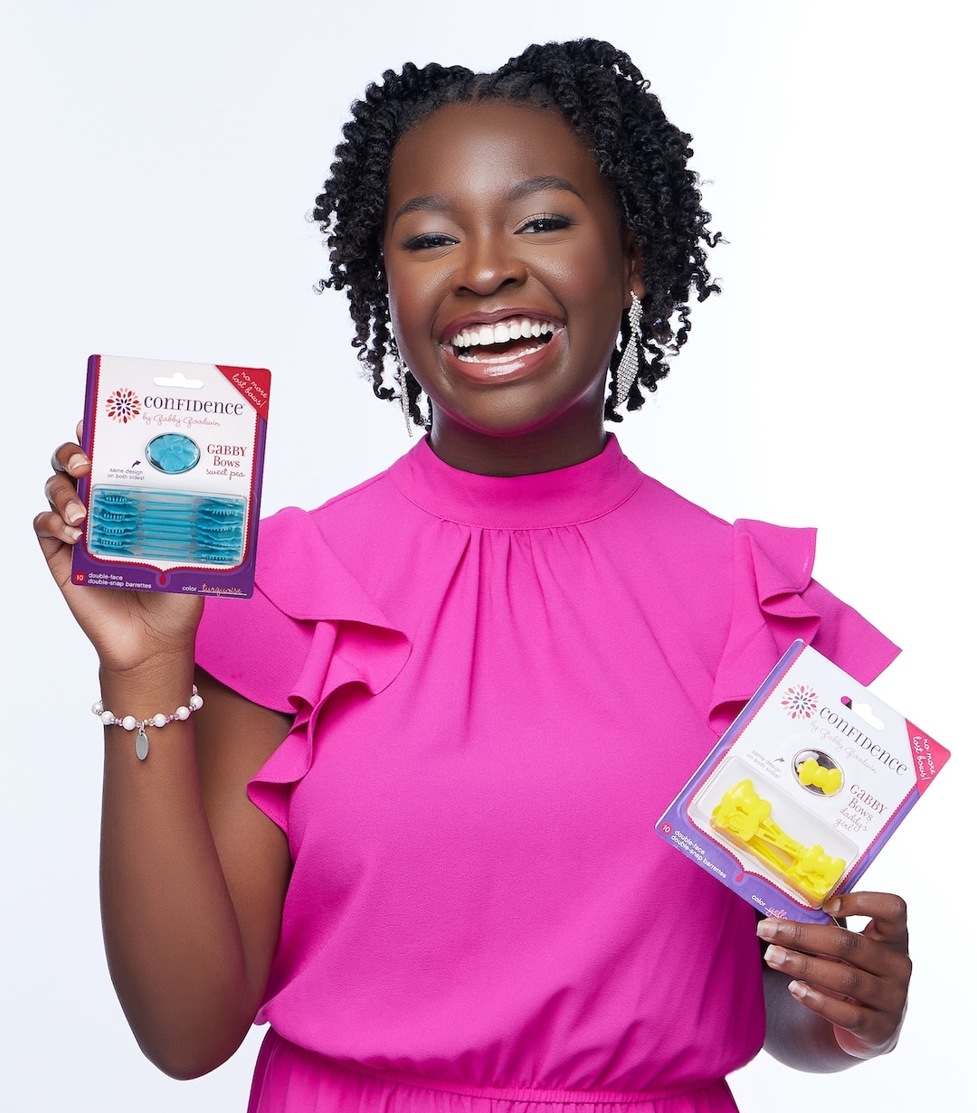 A smiling woman in a bright pink dress holds up two dental care products in colorful packaging, ready to channel your inner artist and sell your craft against a plain white background.