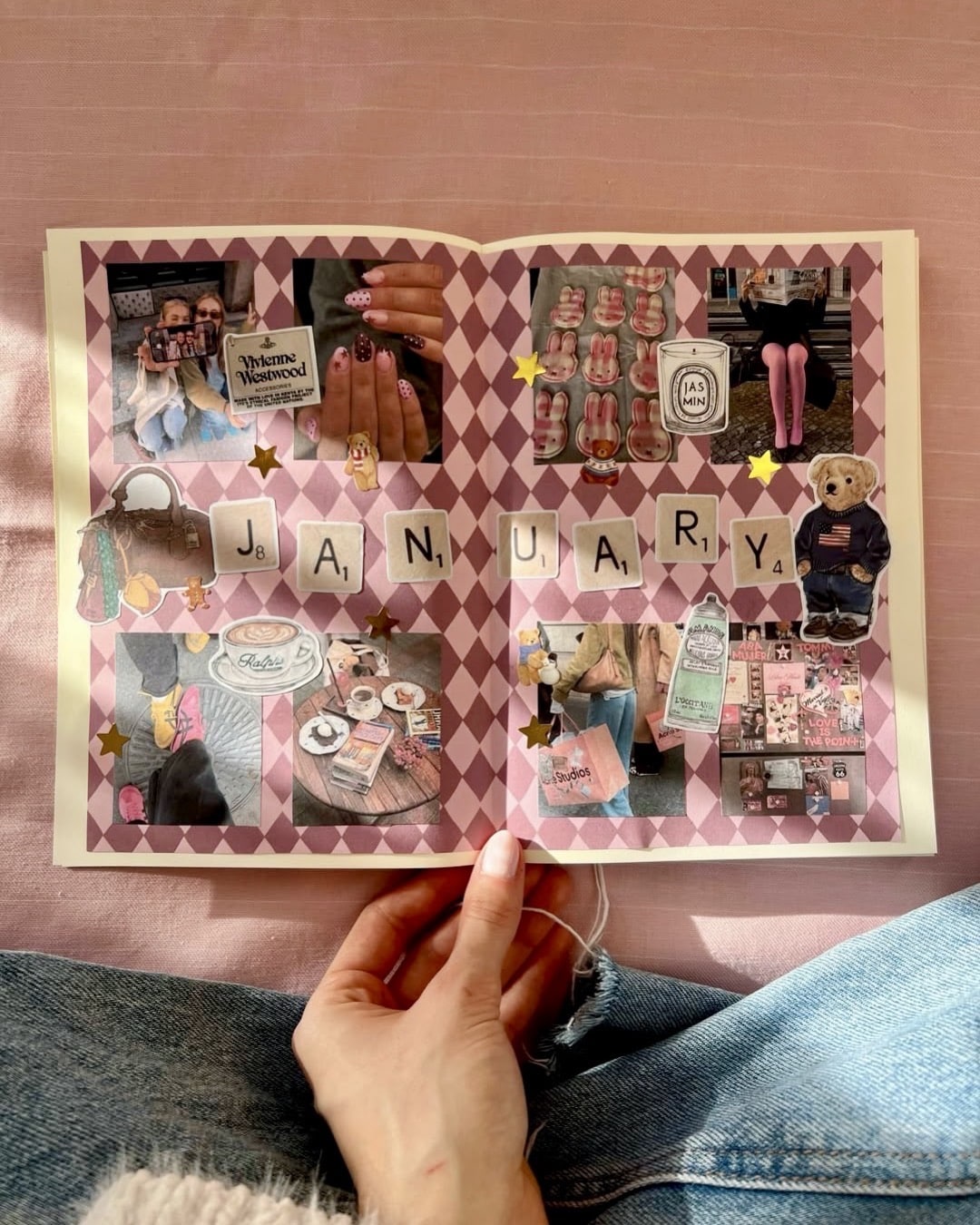 A hand holds open a scrapbook with a pink diamond-patterned background. The pages are decorated with photos, stickers, and cutouts, spelling JANUARY in the center, with various items and images arranged around it.