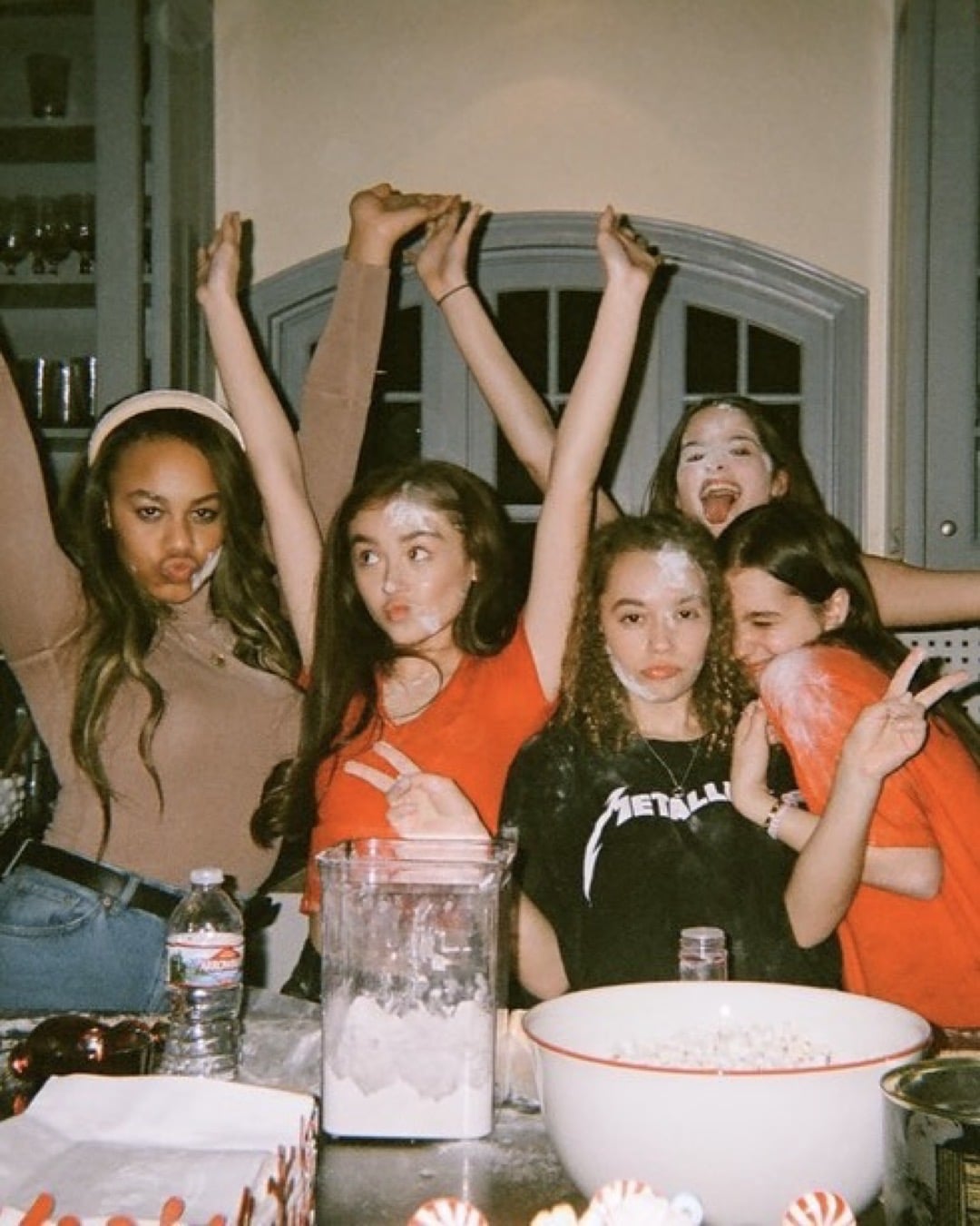 Five girls pose playfully in a kitchen, some with flour on their faces and arms raised. A mixing bowl and kitchen items hint at baking—a perfect scene for family bonding and making memories together.