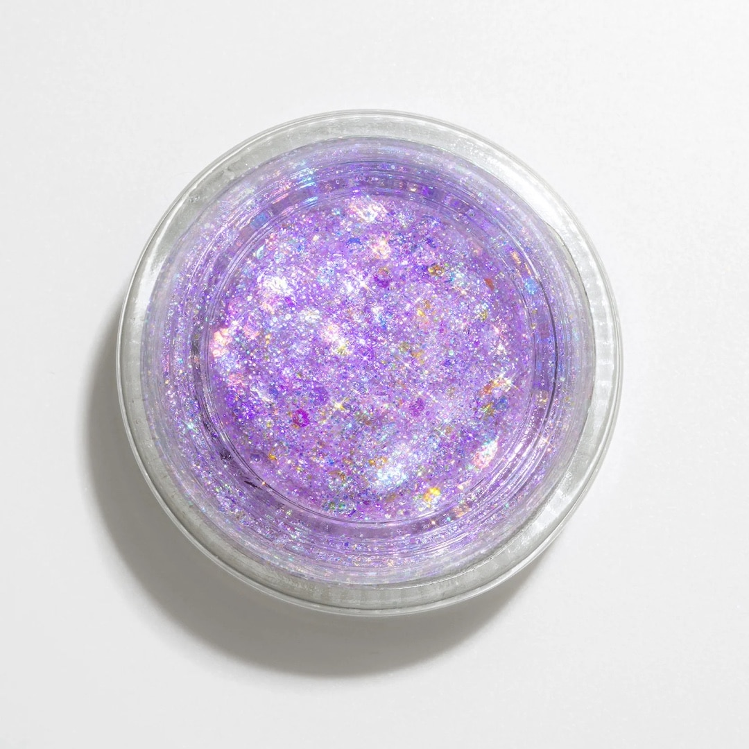 A round container filled with sparkly, iridescent purple glitter gel—perfect for a Taylor Swift-inspired full-glam look—is shown from above on a white background.
