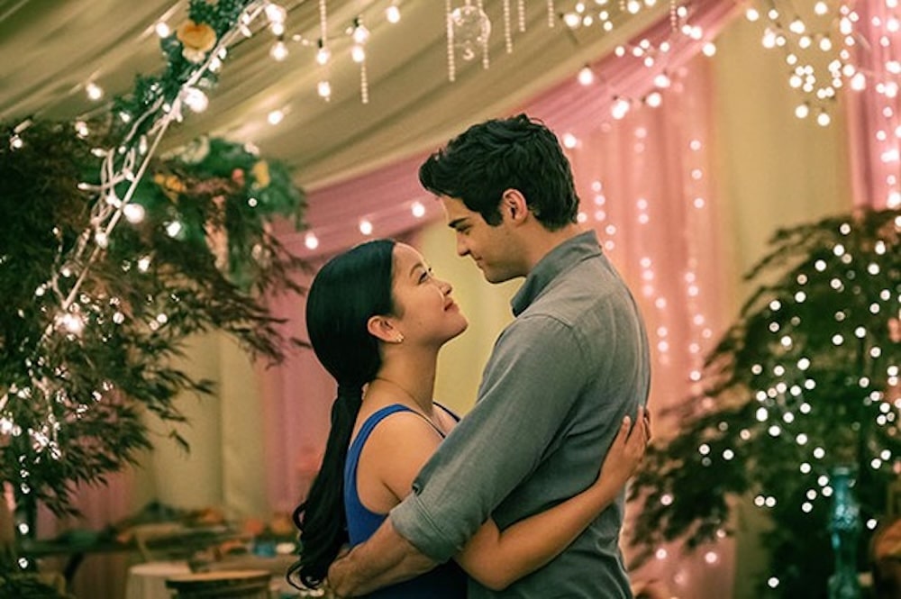 A couple embraces and gazes into each other's eyes while dancing under twinkling string lights and draped fabric at a romantically decorated indoor Galentine's Day celebration.