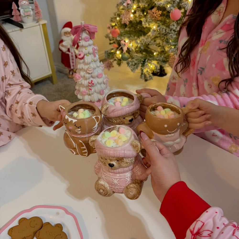 Three BFFs in festive pajamas hold mugs of hot chocolate shaped like bears and gingerbread men during an aesthetic Christmas sleepover. A decorated Christmas tree and cookies complete the cozy background.