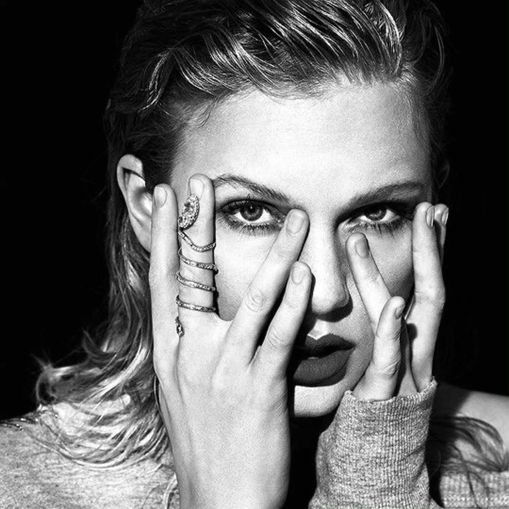 Black-and-white photo of a person with wet hair staring intensely at the camera, covering part of their face with their hands, wearing rings and a long-sleeved top, giving off mysterious zodiac sign vibes.
