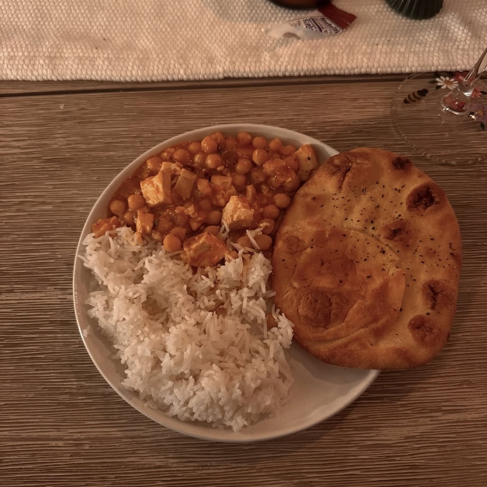 A plate with white rice, chickpea and tofu curry, and a piece of naan bread on a wooden table—perfect comfort food for a rest or reset on a sick day.