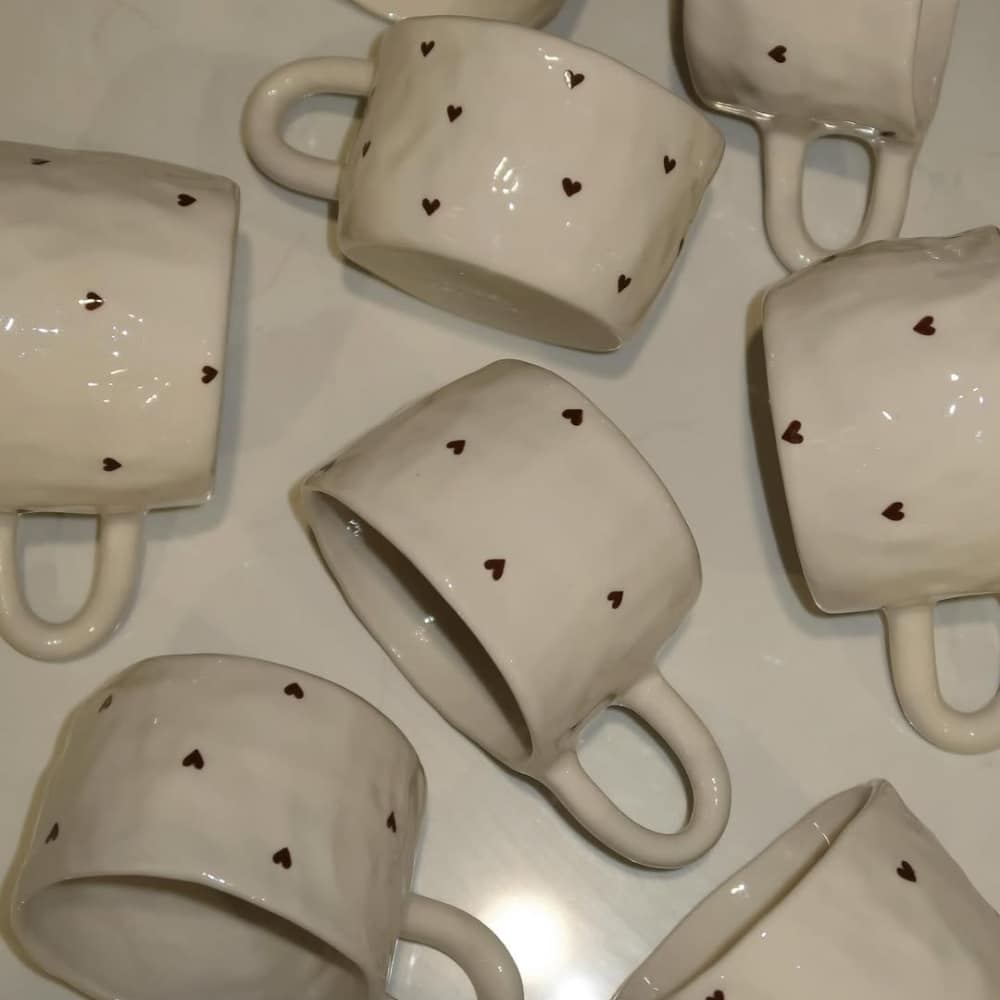 Seven white ceramic mugs with small brown heart patterns are arranged on a light surface, inviting you to reset and relax—perfect companions for a cozy rest or a comforting sick day.