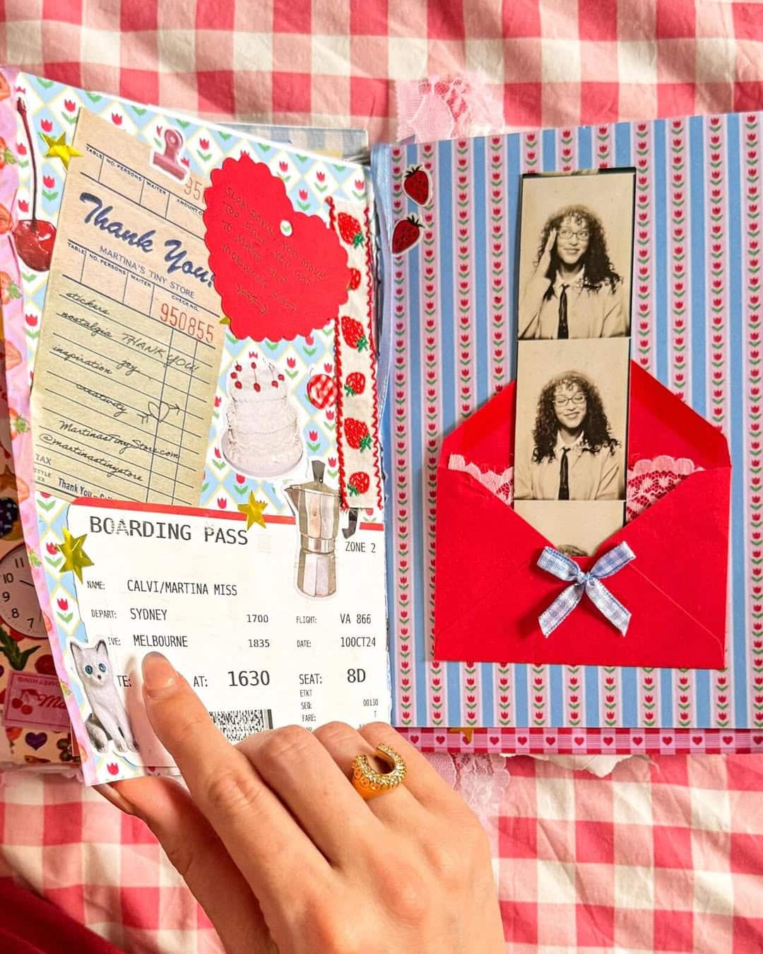 A hand with a ring points to a scrapbook page, featuring a boarding pass, receipt, stickers, and a red envelope with black-and-white photo booth images, all on a red-and-white checkered tablecloth.