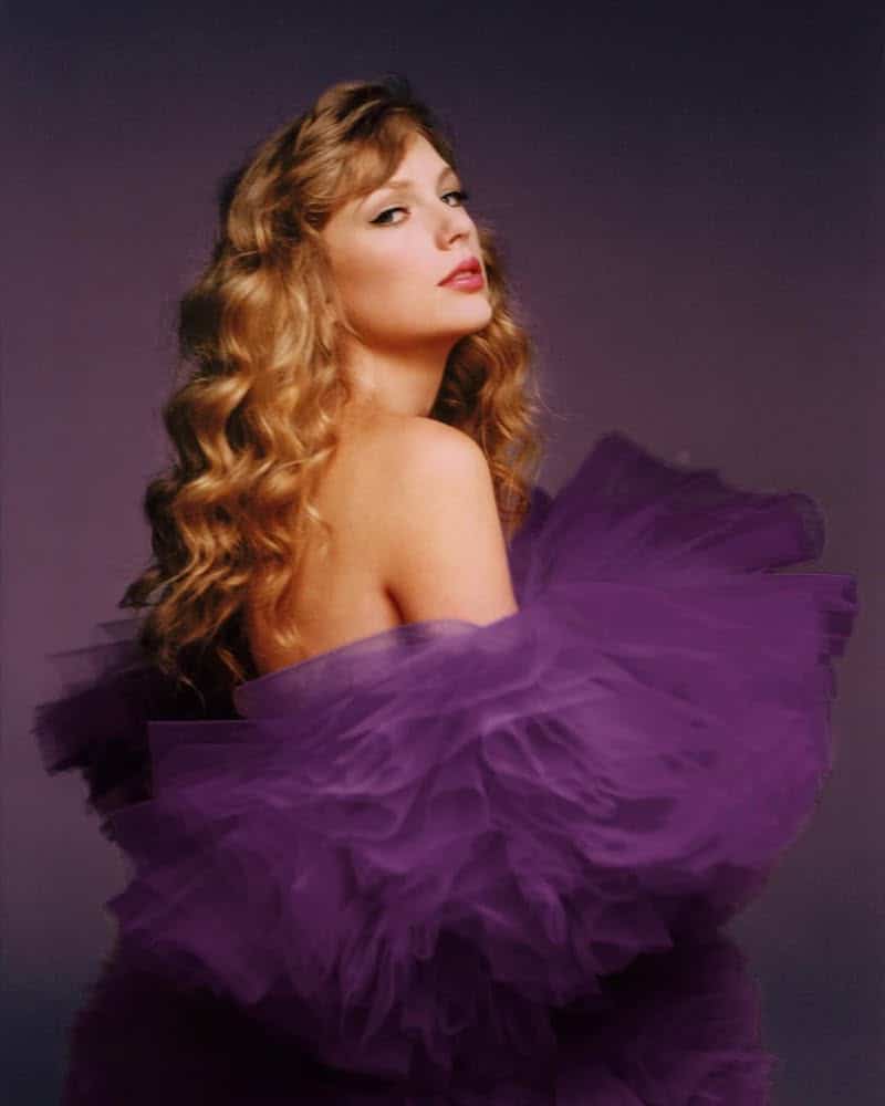 A woman with long, wavy blonde hair poses against a dark background in a dramatic, ruffled purple tulle dress, her serene, confident glance reminiscent of a Taylor Swift album cover.