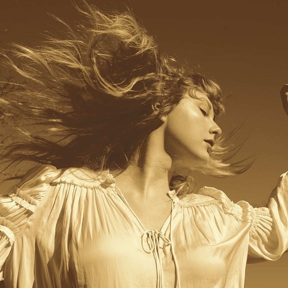 A woman with long hair wearing a light, loose blouse tilts her head back as her hair flows in the wind. The image has a sepia tone, giving it a warm, nostalgic feel.