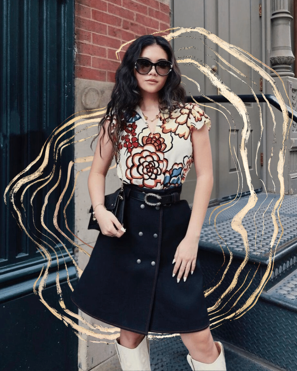 A woman wearing sunglasses, a floral patterned top, and a black skirt stands on a city street near a brick wall and metal steps. Light-colored artistic swirls are drawn around her.